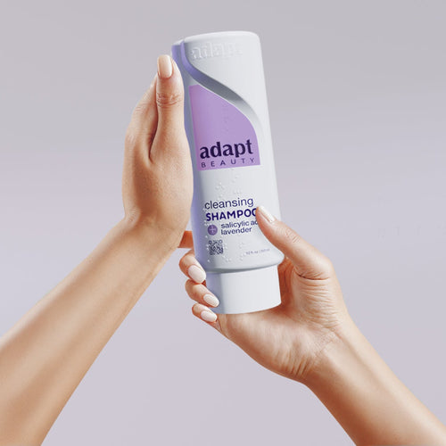 Person holding a bottle of Adapt shampoo against a plain background
