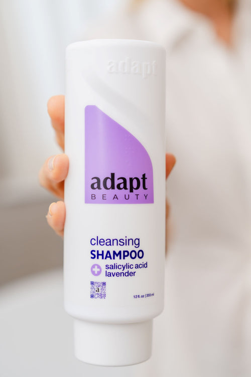 Adapt Beauty cleansing shampoo bottle held by a person with a blurred background